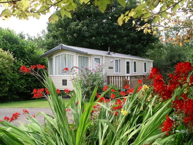 A view of a holiday home with woodland behind and flowers in the foreground