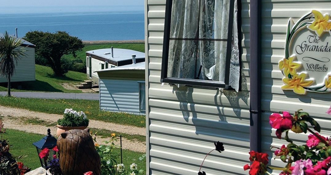 A view of the distant ocean from the side of a holiday home with some beautiful flowers nearby 