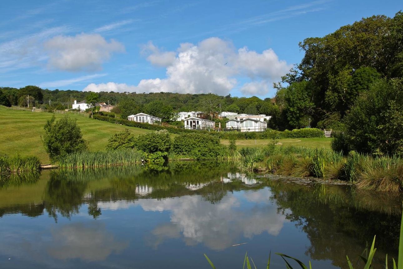 A lake in the foreground with fields and holiday homes in the background
