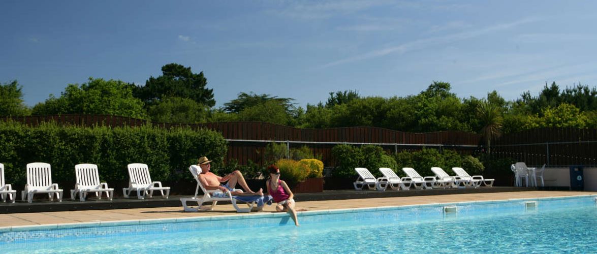 A couple sat next to a swimming pool on a warm sunny day