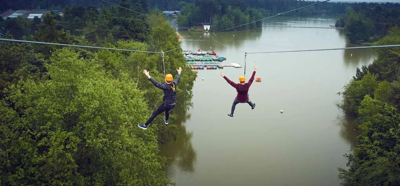 Two people on zip lines travelling over a lake