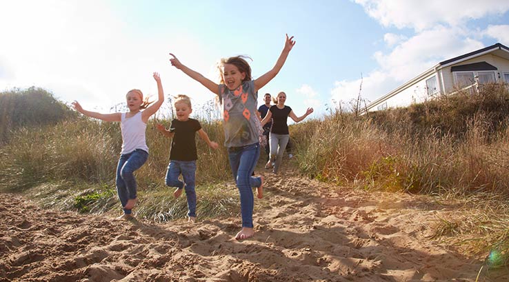 A family running onto the beach from a holiday park