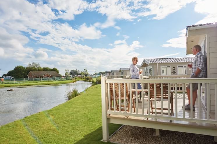 A couple standing on their holiday home outside decking area near the lake