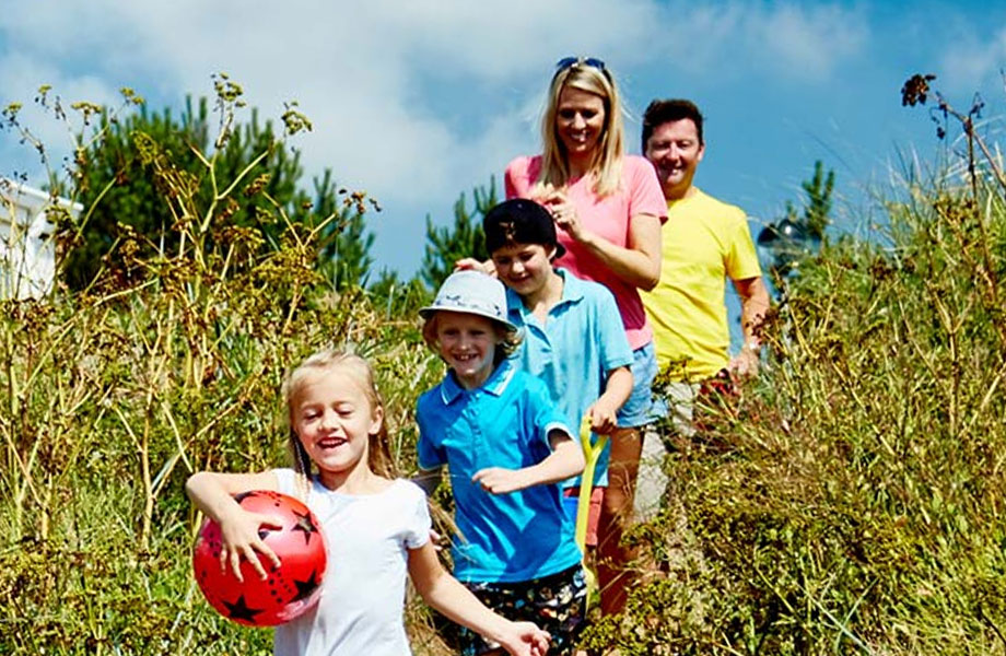 A family running towards the sea through tall grass