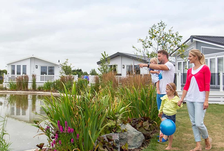 A family walking through a holiday park past holiday homes near a lake