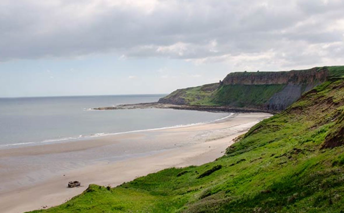 An image of green rolling hills down to a beach