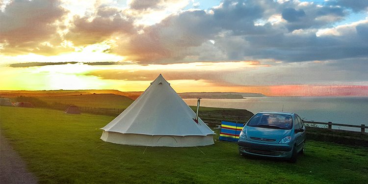 An image of a car and tent overlooking the sea as the sun is setting