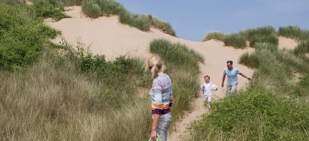 A family walking through sands dunes on a bright and warm summers day
