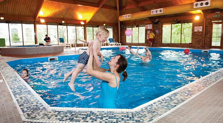 A parent lifting their child up out of the water inside an indoor pool