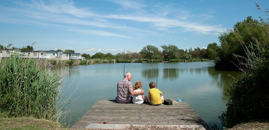 Children and an Adult Sitting on a Jetty Fishing on a Lake near to Holiday Homes