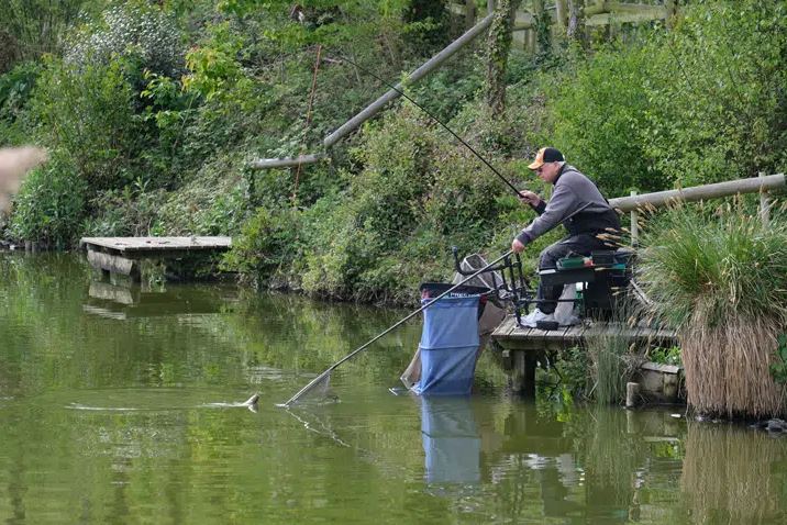 An Image of a Man sat down Landing a Fish at the Lakeside