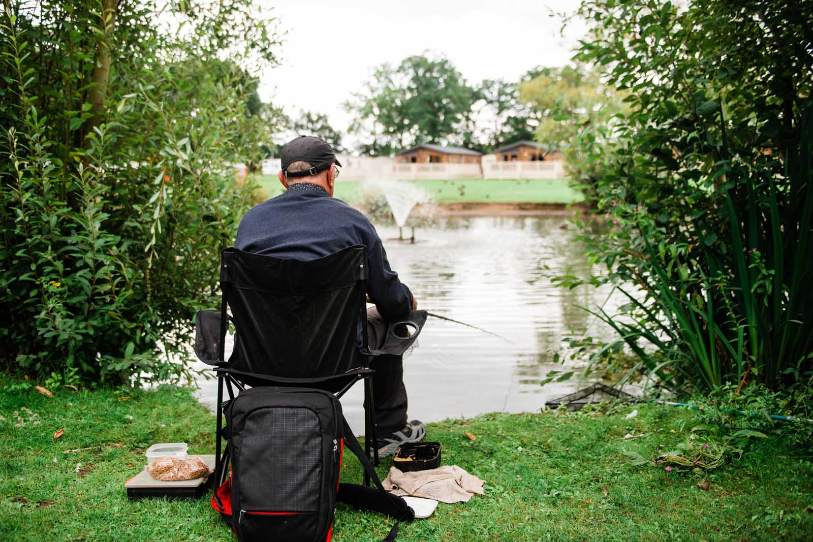 A Man Fishing Whilst Sat Down next to a Lake on a Holiday Park