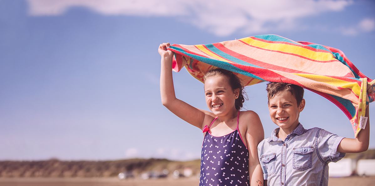 Two Children Holding a Towel Above their Heads on a Beach