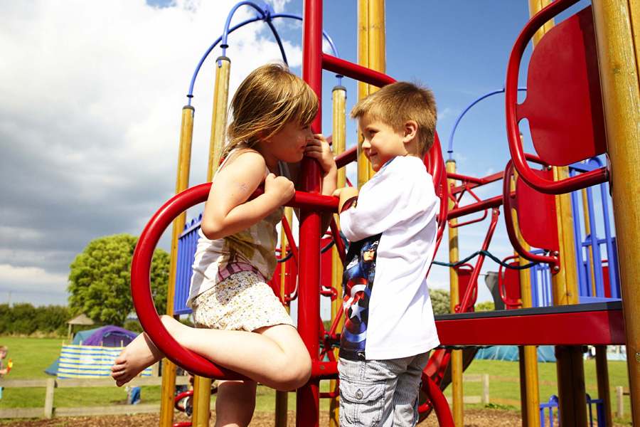 Two Children Talking Whilst Playing on a Play Park Outside on a Bright Sunny Day