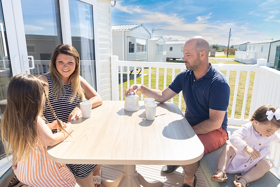 A Family of Four Sat at a Table on the Decking of their Holiday Home on a Bright Sunny Day