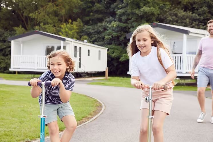 Two Children on Scooters Riding away from an Older Male Family Member who is Laughing