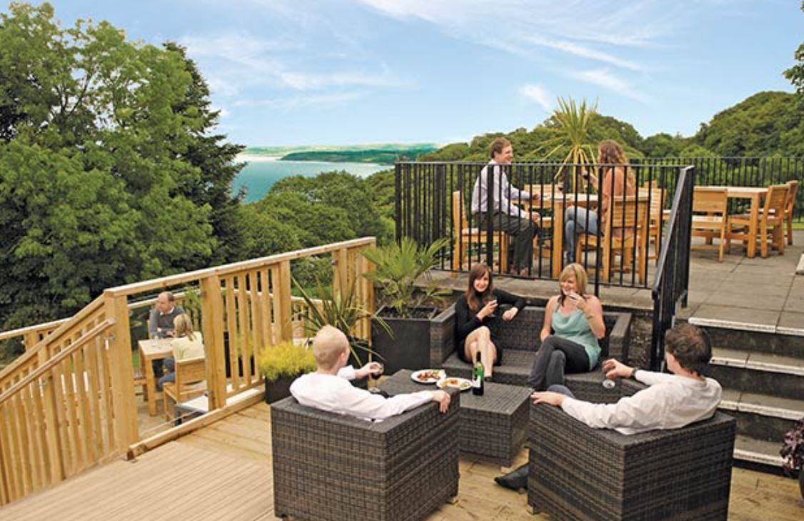 An Image of People Enjoying Refreshments on a Terrace Overlooking the Woods and Sea