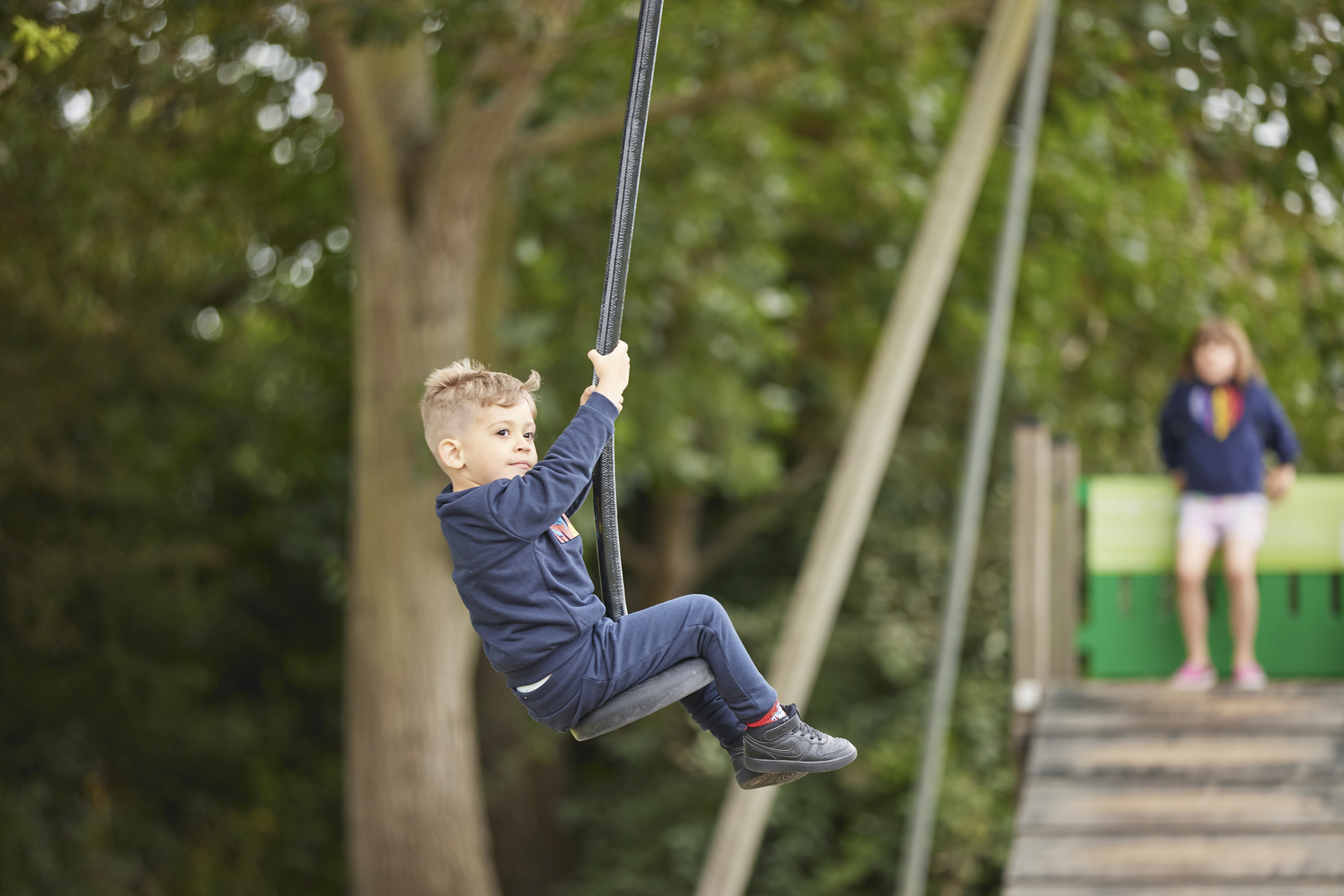 A Child Swinging Along a Zip Line Near a Tree with Another Child Watching