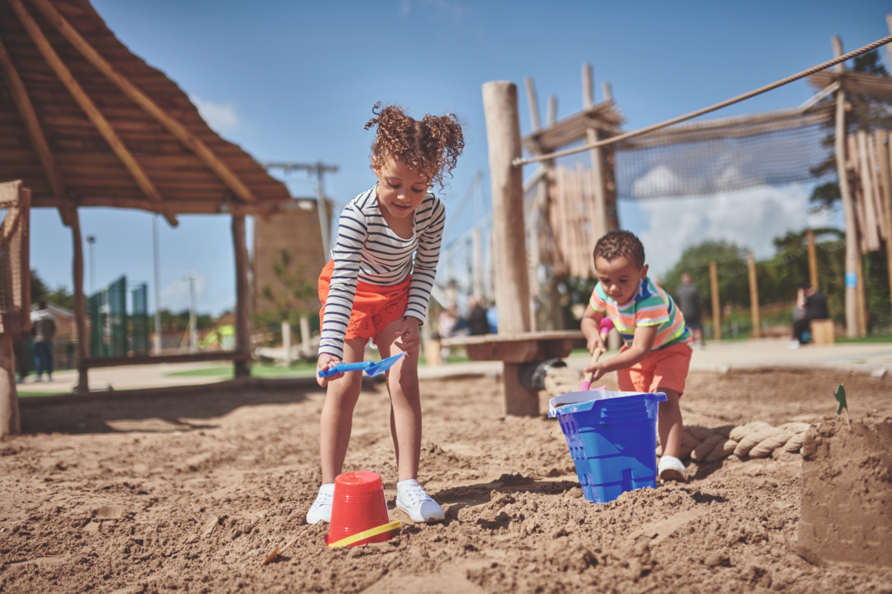 Children Playing in a Sand Pit with Wooden Climbing Structures in the Background