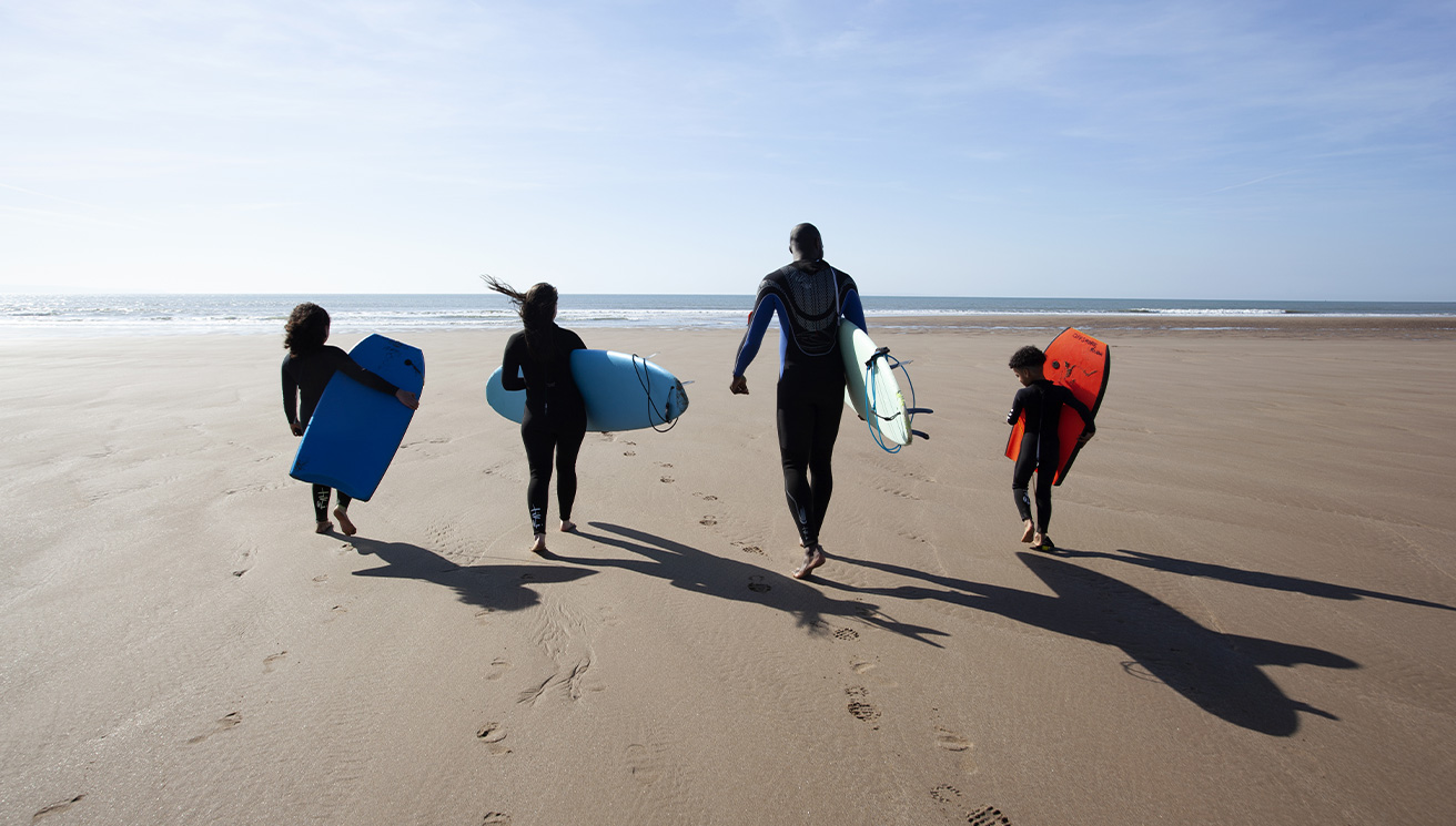 Four People Walking on a North Devon Beach with Surfboards and Bodyboards