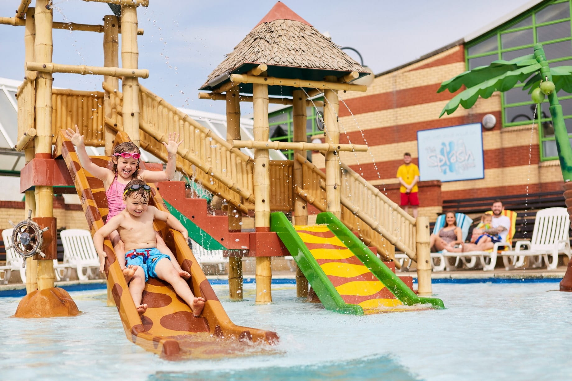 Two Children on a Water Slide in a Outdoor Swimming Pool Area