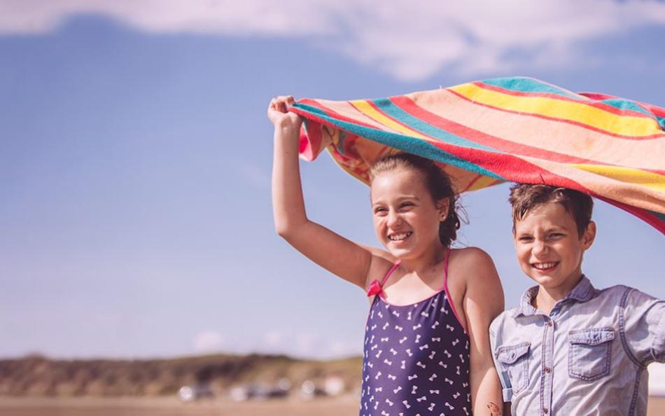 Two children holding a towel above their heads on a beach