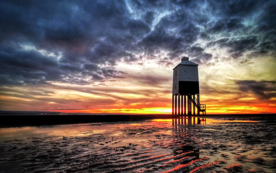 A lighthouse at sundown with the tide still out and reflections on the wet sand