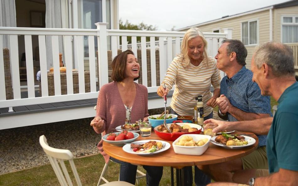 Two couples eating food at a table in front of their holiday homes