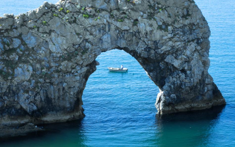 A crystal blue ocean with a boat viewable through a cave  on a warm sunny day