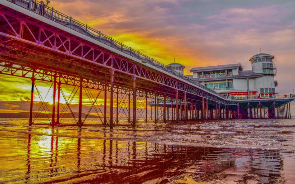 A pier as the sun is setting and reflecting off the water and sand