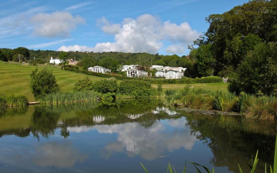 A lake in the foreground with fields and holiday homes in the background