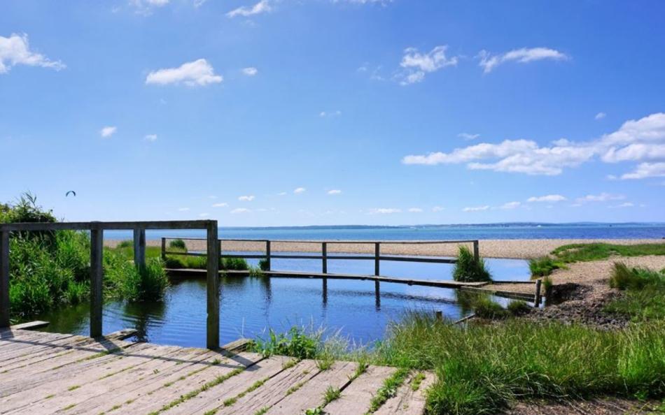 A view of a Hampshire beach with blue skies and a river with a bridge over reflecting the sky