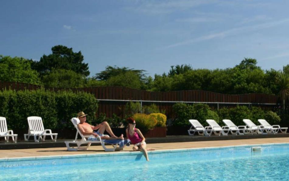 A couple sat next to a swimming pool on a warm sunny day