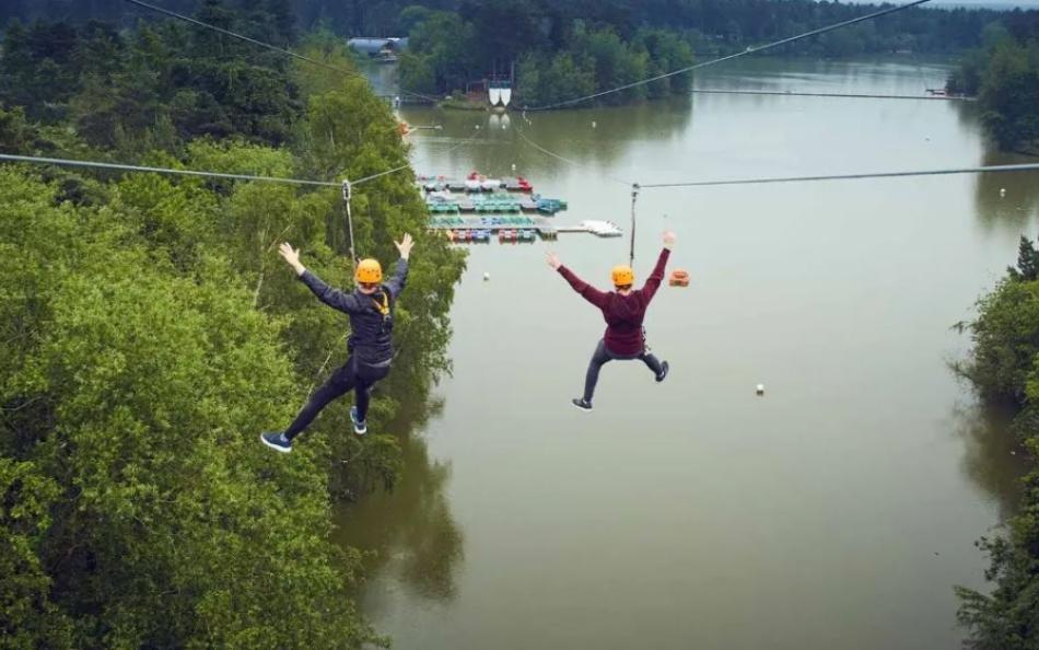 Two people on zip lines travelling over a lake