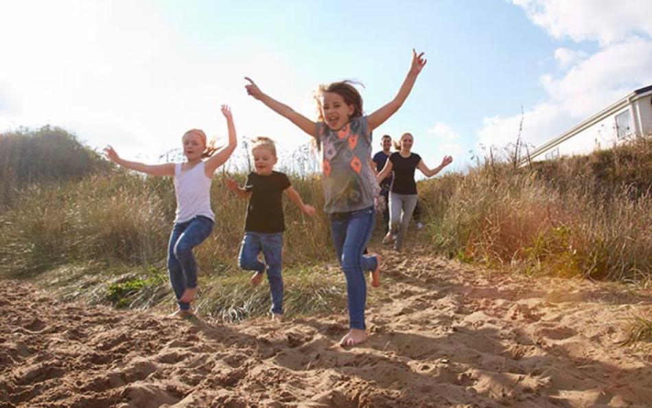 A family running onto the beach from a holiday park