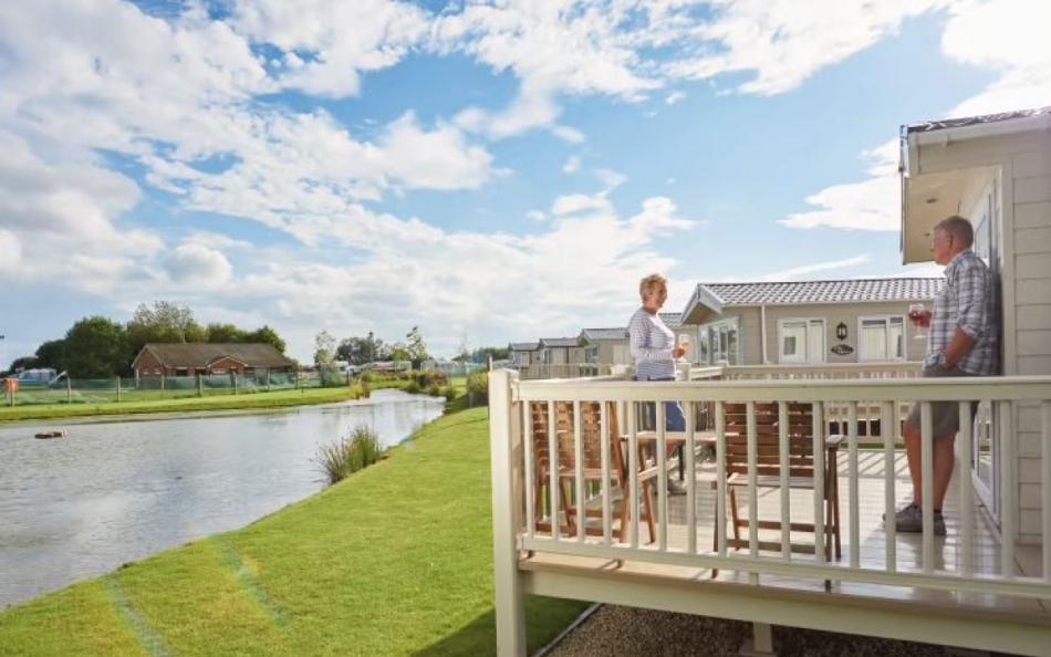 A couple standing on their holiday home outside decking area near the lake