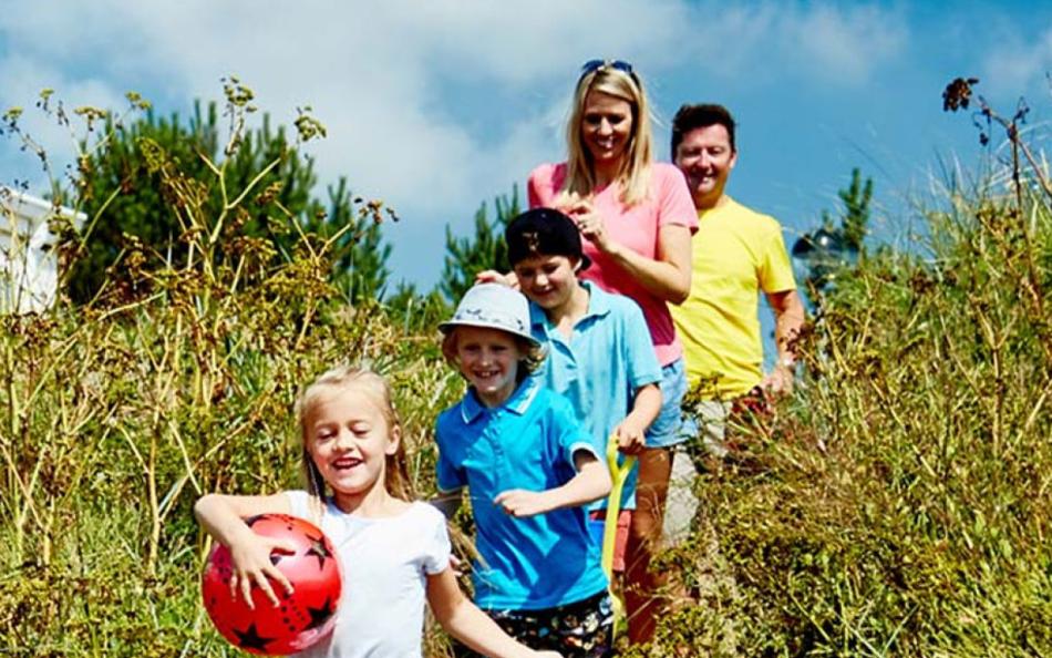 A family running towards the sea through tall grass