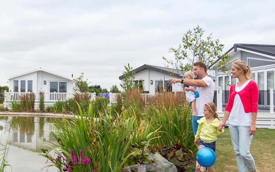 A family walking through a holiday park past holiday homes near a lake