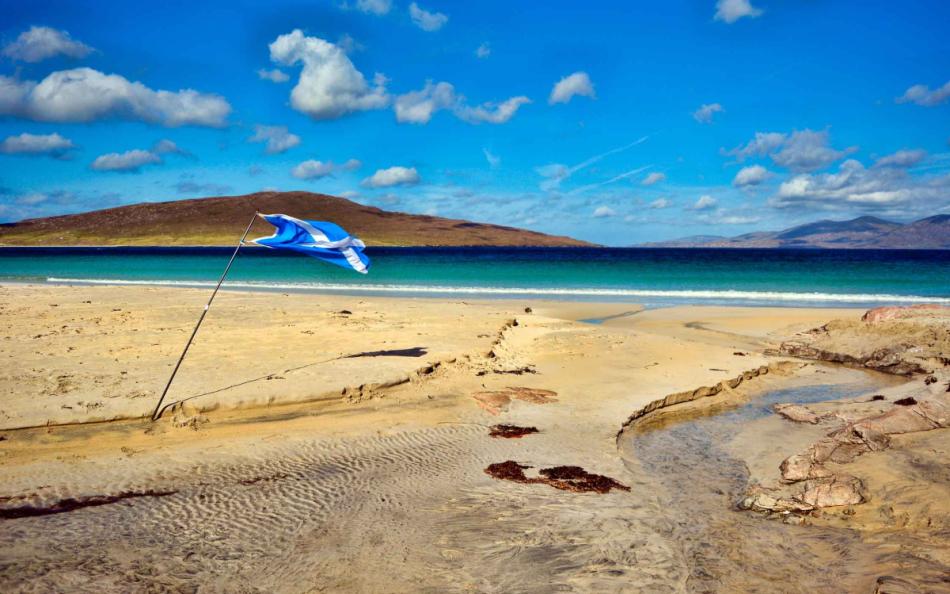  A deserted beach, golden sands and blue sky, with a Scottish flag placed in the sand