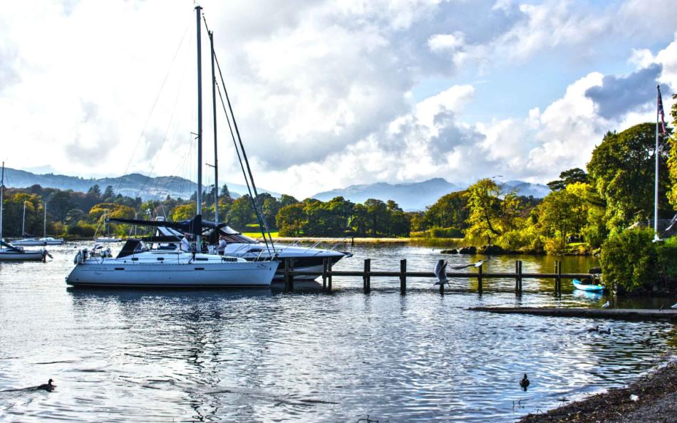 People aboard a yacht on a lake surrounded by other boats and forests