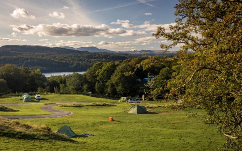 A view of a lake in the far distance and a rolling hill leading down to the shore in amongst trees