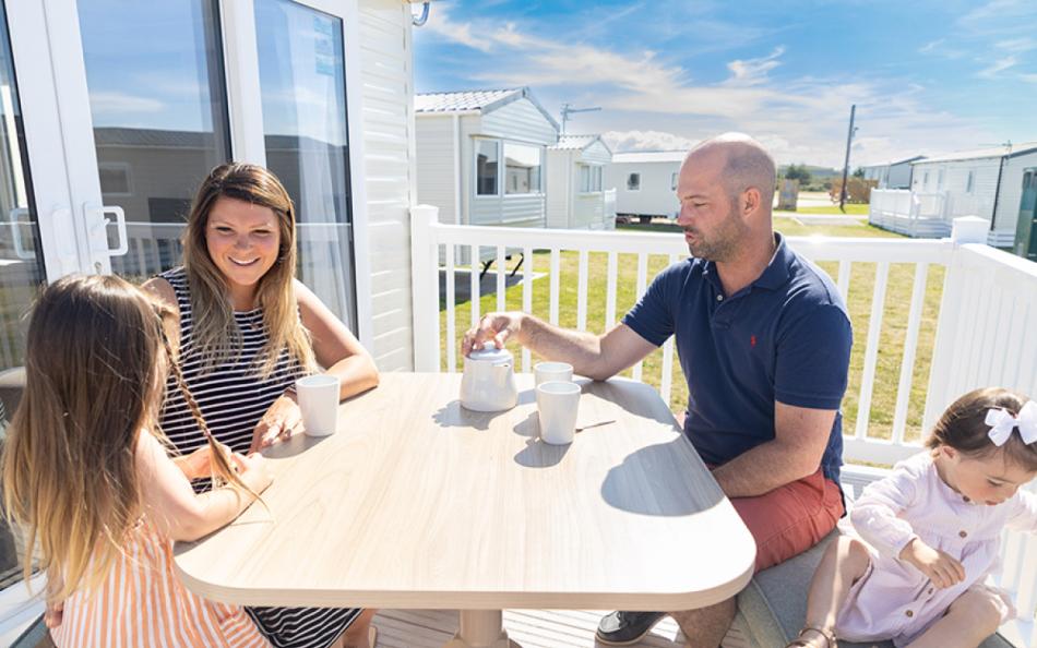 A family of four sat at a table on the decking of their holiday home on a bright sunny day