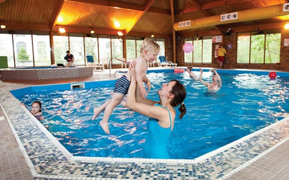 A parent lifting their child up out of the water inside an indoor pool