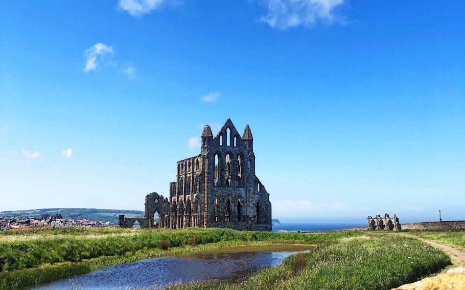 An image of Whitby Abby with the coastline in the distance on a bright sunny day