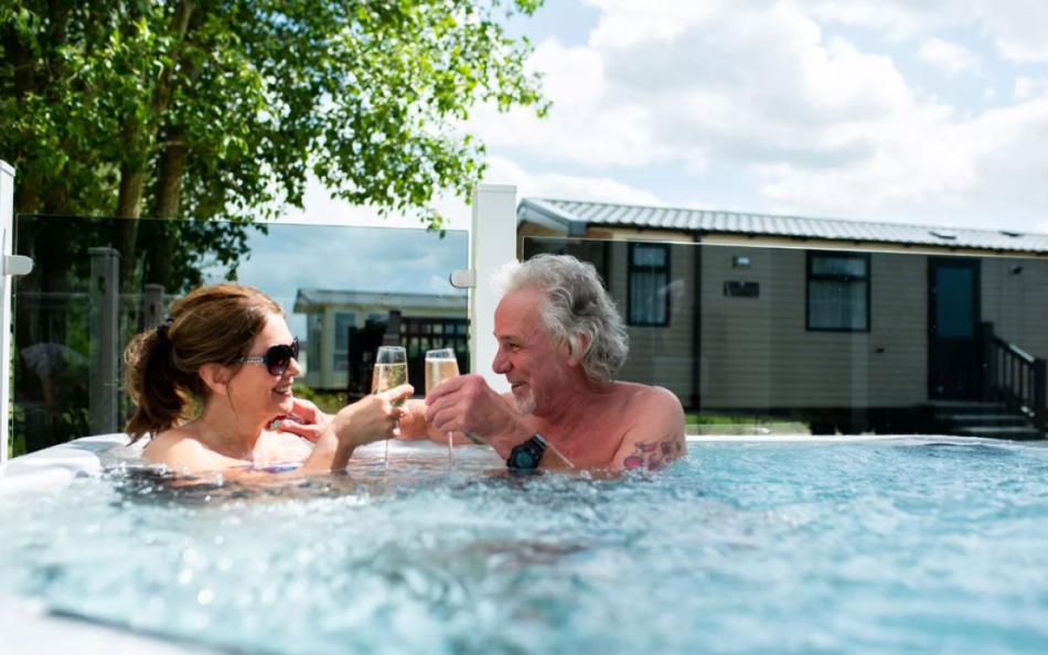A Middle Aged Couple Enjoying a Glass of Champagne in a Hot Tub next to their Holiday Home 