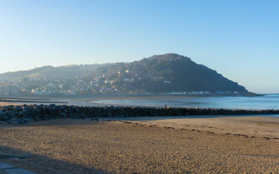 An Image of a Somerset Beach with a Local Town set against a Wooded Hill