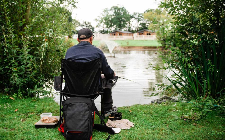 A Man Fishing Whilst Sat Down next to a Lake on a Holiday Park