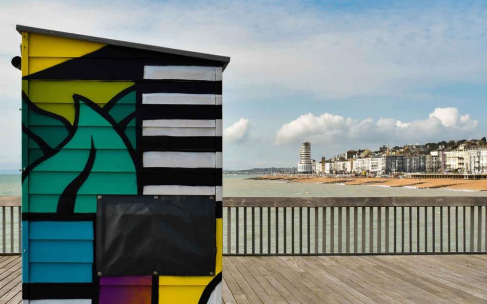 A Grafitti'd Wooden Cabin on A Pier Overlooking the Beach and Town in the Background