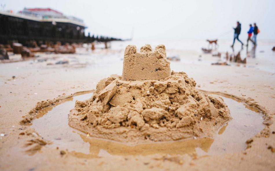 A Sandcastle on a Beach with People Walking in the Background