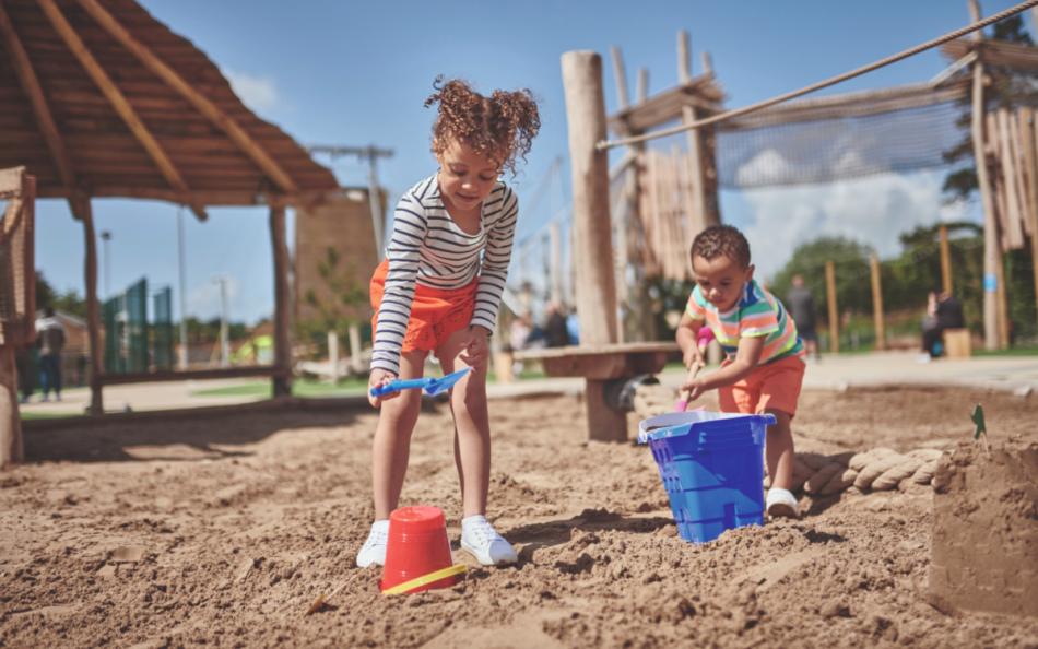 Children Playing in a Sand Pit with Wooden Climbing Structures in the Background